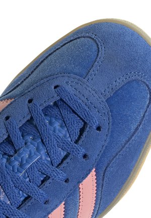 Gros plan d'une basket en daim bleu avec des rayures roses, des lacets bleus et une languette bleue texturée.