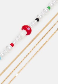 Colar de contas coloridas com uma conta em forma de cogumelo vermelho, pérolas brancas e pretas, juntamente com três correntes de ouro finas com texturas variadas.