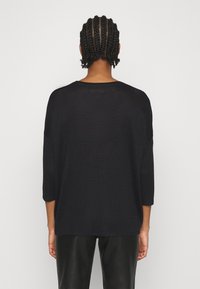 Czarny sweter z dzianiny, luźny krój z rękawami 3/4 i okrągłym dekoltem. Miękka tekstura, minimalistyczny design, odpowiedni na codzienne noszenie.