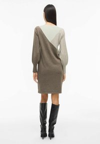 Abito a maglia marrone e grigio con un design a blocchi di colore geometrici, maniche a palloncino e orlo al ginocchio. Indossato con stivali neri al ginocchio.
