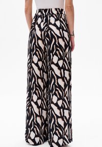 Wijde broek met een abstract patroon in zwart, wit en bruin. Gemaakt van lichtgewicht stof met een elastische tailleband voor comfort.