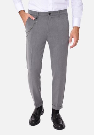 Pantaloni grigi su misura con un design aderente, caratterizzati da un accento a catena sulla tasca e abbinati a mocassini neri.