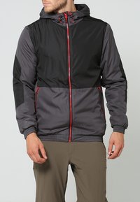 Giacca leggera grigia e nera con accenti rossi, chiusura con zip, cappuccio e polsini elasticizzati. Tessuto liscio con pannelli a contrasto.