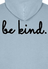 Ljusblå hoodie med en mjuk textur som pryder texten "var snäll." i fet svart, kursiv brodyr på baksidan.
