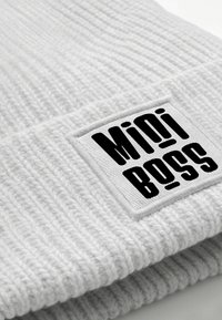 Gray knitted beanie with a ribbed texture, featuring a rectangular white patch displaying the text "Mini Boss" in bold black font.