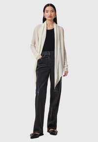 Ljus beige �öppen cardigan, ribbad textur, långa ärmar, matchad med svarta läder byxor med vida ben och svarta platta skor med guldaccenter.