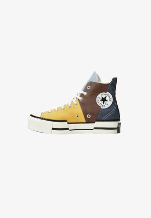 Hoge sneakers met gele, bruine en marineblauwe canvas delen, een witte rubberen zool, zwarte strepen en een opvallend sterlogo.