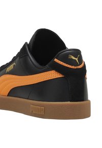 Sneaker nera in pelle con dettagli in suede arancio e suola in gomma naturale. Presenta il marchio Puma dorato sul tallone e sul lato.