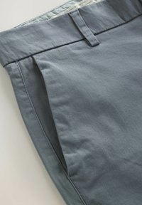 Pantalones de algodón grises con frente plano, que presentan bolsillos laterales y una cintura texturizada. Tela suave con un ligero brillo.