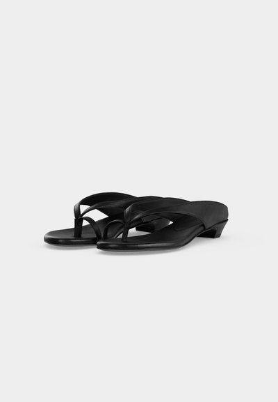 Ζευγάρι μαύρα σανδάλια με χαμηλό τακούνι, φαρδιά λουράκια και ανάμεσα στα δάχτυλα, εμφανίζονται σε απλό ανοιχτογκρι φόντο.