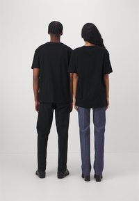 T-shirt di cotone nera indossata da due persone, una abbinata a jeans neri e l'altra a pantaloni a righe blu, viste da dietro.