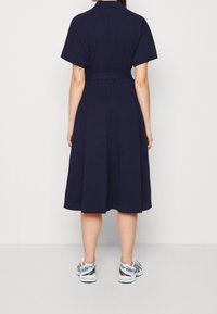 Mörkblå midi-klänning med korta ärmar, bälte i midjan och utsvängd kjol. Buren tillsammans med ljusgrå och blå löparskor. Slät, enfärgad tyg.