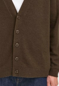 Brown cardigan featuring a textured knit, v-neck design, and six dark buttons along the front, paired with a white shirt underneath.