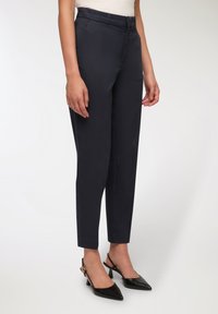 Marynarskie spodnie wykonane z gładkiego materiału, o dopasowanym kroju, wysokim stanie i zwężających się nogawkach; w połączeniu z czarnymi szpilkami z odkrytymi piętami i szpiczastymi noskami.