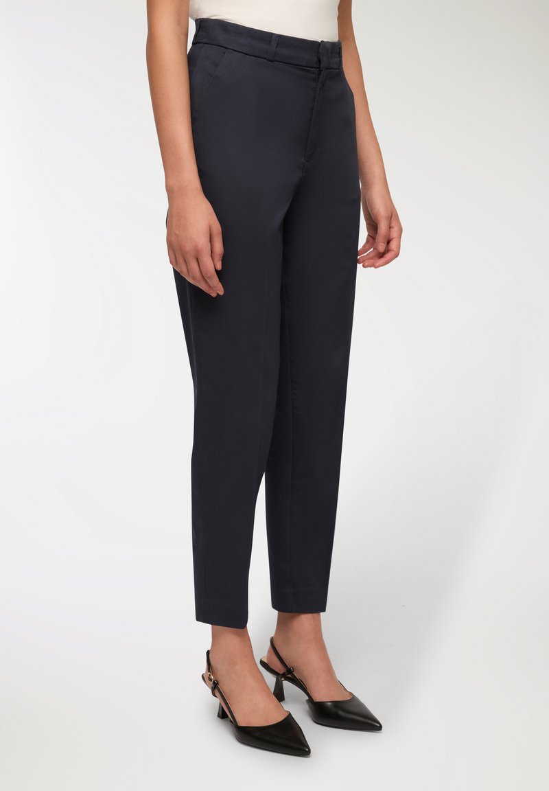 Marynarskie spodnie wykonane z gładkiego materiału, o dopasowanym kroju, wysokim stanie i zwężających się nogawkach; w połączeniu z czarnymi szpilkami z odkrytymi piętami i szpiczastymi noskami.
