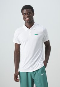 Witte Nike polo met korte mouwen, een kraag en een groene swoosh-logo. Draagt met teal sportshorts. Glad textuur.