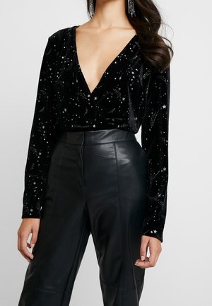 Haut noir en velours à manches longues avec motifs d'étoiles argentées, col en V profond, associé à un pantalon en cuir noir taille haute et de longues boucles d'oreilles pendantes.