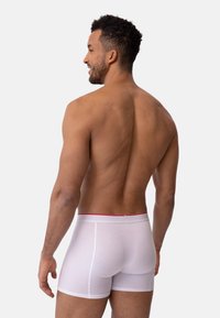 Boxer blancos con una cintura roja, diseño ajustado y textura suave y lisa. Mostrados de espaldas.