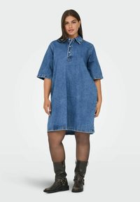 Denimová košilová šaty s límečkem, krátkými rukávy a volným střihem. Mají světle modrou barvu a kontrastní švy. Vytvářejí outfit s černými kotníkovými botami.