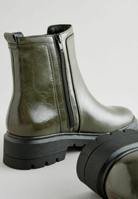 Botas de tobillo de imitación de cuero verde con cremallera lateral, suela negra gruesa y acentos texturizados. Acabado suave y detalle de punta redondeada.