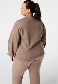 Bruin gebreid sweater met een ontspannen pasvorm, verlaagde schouders en ribbelaccenten, gecombineerd met textuur matching broek in een vergelijkbare tint.