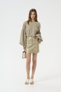 Top in tessuto beige con maniche a sbuffo, mini gonna oro con stampa di serpente, mules bianche con la punta aperta e una borsa abbinata con motivo a serpente.
