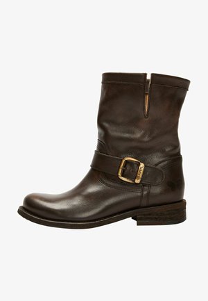 Brown leather ankle boot with a rounded toe, side buckle detail, stitched accents, and a low stacked heel. Features a distinct texture.