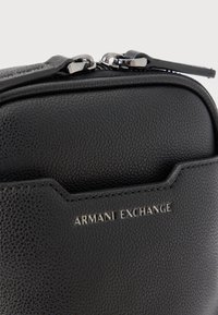 Μαύρο τσαντάκι από δερματίνη Armani Exchange με διπλά ασημένια φερμουάρ και εμφανές λογότυπο της μάρκας μπροστά.