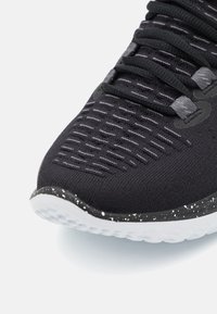 Sort løbesko med en tekstureret strikoverdel, subtile grå mønstre og en hvid spraglet sål. Har elastiske snørebånd og ergonomisk design.