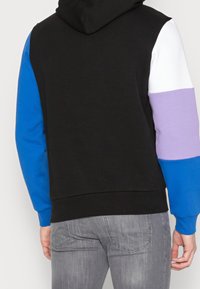 Felpa con cappuccio dal corpo nero, maniche blu e viola, e spalle bianche. Tessuto in misto cotone con polsini e orlo a costine.