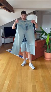 Jeans de ganga azul claro segurados por uma pessoa, com corte reto, costura visível, bolsos padrão e uma etiqueta presa à cintura.