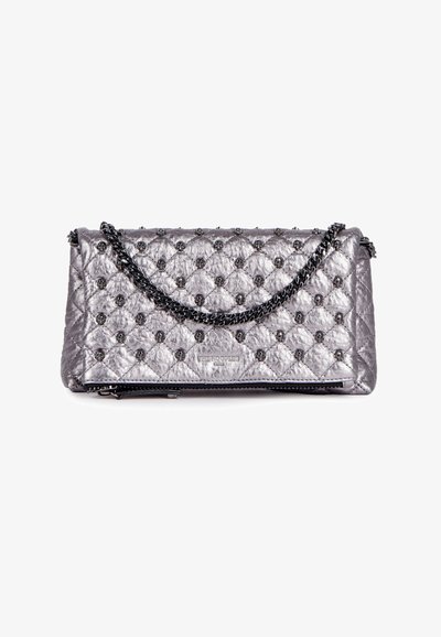 Pochette métallisée argent matelassée avec une chaîne noire, présentant des détails embossés et une fermeture éclair sur le bord inférieur.