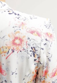 Bloemenprintstof in het wit, met roze, oranje en paarse bloemen en delicate groene accenten. Gladde textuur, ontspannen ontwerp en schouderdetails.