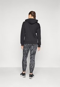 Felpa nera con tasca sul retro, abbinata a leggings grigi con stampa leopardata e strisce laterali nere, accompagnati da scarpe da ginnastica nere.