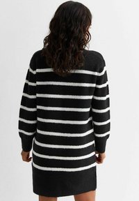 Robe pull tricotée en noir avec des rayures horizontales blanches, dotée de manches longues, d'une coupe décontractée et d'échancrures sur les côtés à l'ourlet.