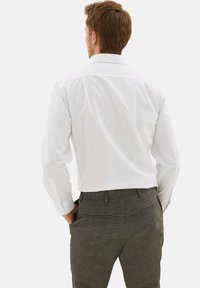 Camisa blanca de manga larga con cuello estándar y textura suave, combinada con pantalones grises con un patrón de diseño a cuadros.