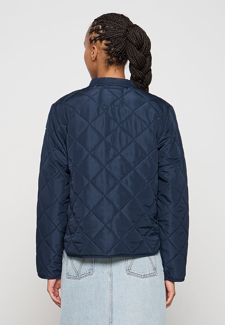 Chaqueta acolchada de color azul marino con un patrón de diamante, cuello redondo y mangas largas; fabricada con un tejido suave y ligero.