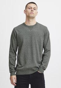 Suéter de algodón verde oscuro con mangas largas, cuello redondo, acentos de punto texturizado y un ajuste ligeramente holgado. Diseño liso, sin patrones ni herrajes.