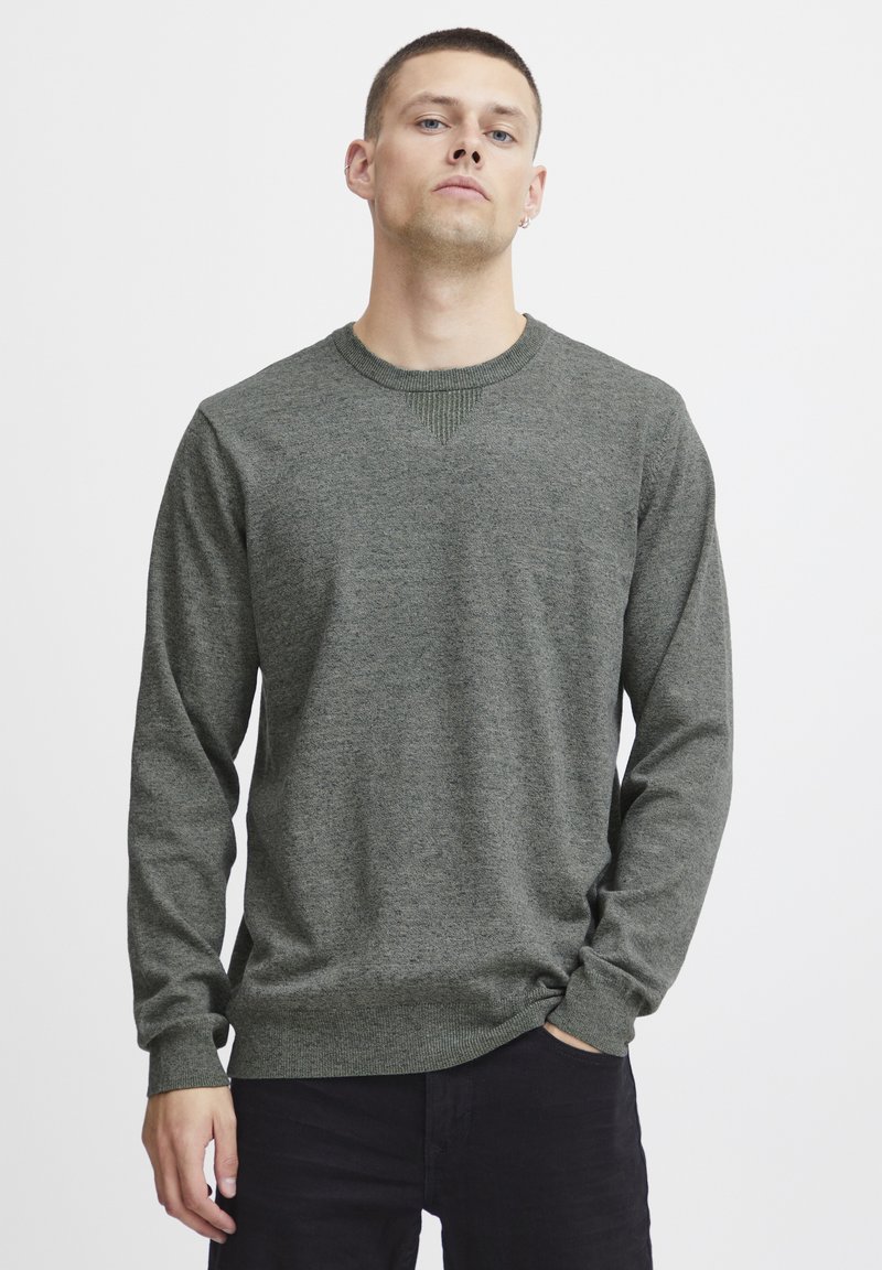 Suéter de algodón verde oscuro con mangas largas, cuello redondo, acentos de punto texturizado y un ajuste ligeramente holgado. Diseño liso, sin patrones ni herrajes.