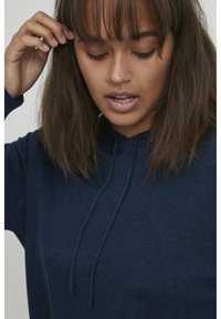Sudadera azul marino de tela suave, con capucha ajustable y puños acanalados, de corte relajado y detalles de costura mínimos.