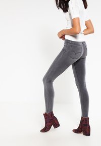 Jeans skinny grigi con vita media, abbinati a stivaletti alla caviglia a fantasia in rosso scuro e viola. Top bianco corto a maniche corte con texture.