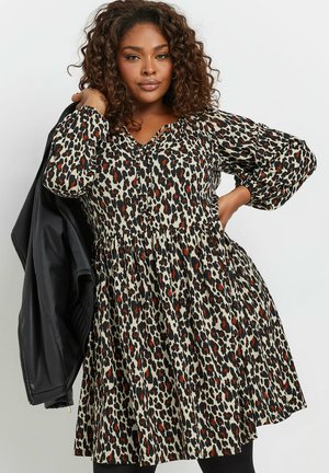 Leopardprint kjole i beige, sort og rød med V-hals, puffede ærmer og en indsnævret talje. Akkompagneret af en sort læderjakke.