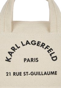 Beige vászontáska fekete felirattal, amelyen az "KARL LAGERFELD PARIS" és a cím szerepel. Masszív fogantyúk, texturált felülettel.