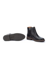 Des bottes ankle en cuir noir présentent une fermeture éclair sur le côté, un bout rond et un talon empilé. La semelle a une texture antidérapante pour une meilleure adhérence. L'intérieur est de couleur beige.