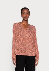 Blusa de manga longa vermelha com decote em V, apresentando um tecido leve e texturizado e um corte solto. Acentuada com pequenos padrões brancos e pretos.