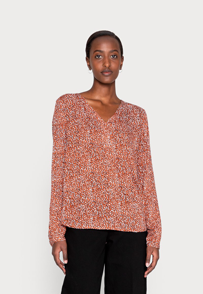 Blusa de manga longa vermelha com decote em V, apresentando um tecido leve e texturizado e um corte solto. Acentuada com pequenos padrões brancos e pretos.
