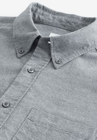 Grijze flanellen shirt met een button-down kraag, voorzien van twee grijze knopen en een borstzak aan de linkerkant; zachte textuur met een gladde afwerking.