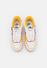 Pair of white Nike Air Force 1 sneakers with yellow, red, green, and blue accents viewed from above on a white background.