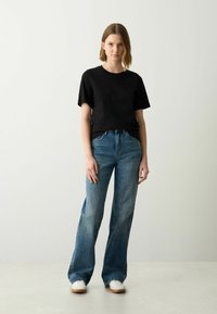 Zwarte T-shirt met korte mouwen gecombineerd met lichtblauwe, wijde jeans. De jeans hebben een vervaagde wassing en subtiele stikseldetails. Witte sneakers maken de outfit compleet.