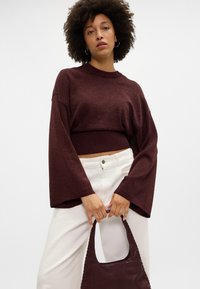 Sweater curto bordeaux com tecido texturizado e mangas largas, combinado com calças brancas de cintura alta e uma bolsa bordeaux.